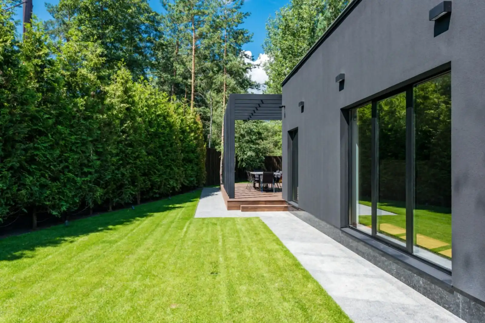Dark modern house exterior with tall glass doors opening onto a lawn