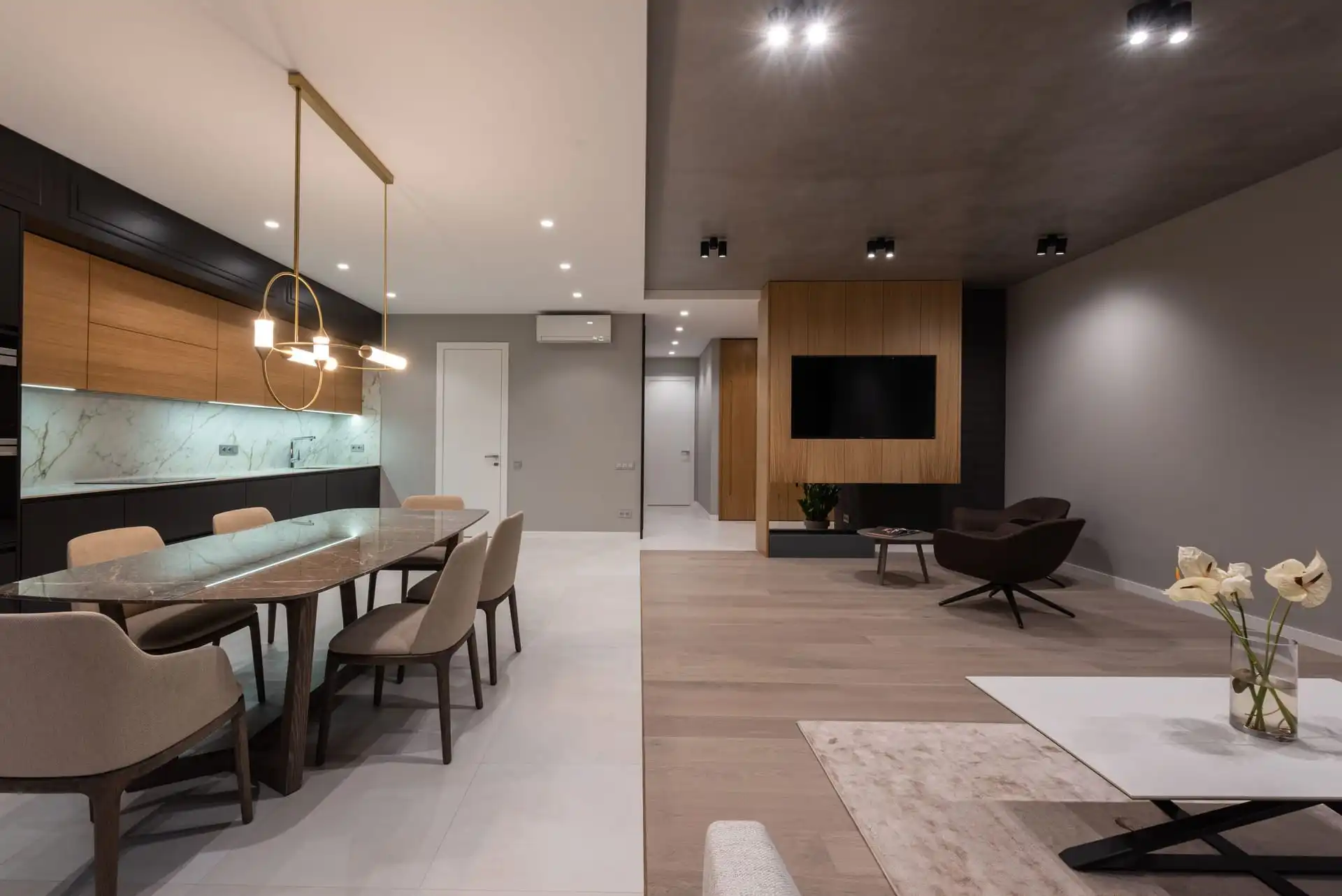 Open-plan dining and living room with a long marble table, pendant lights and a timber TV wall