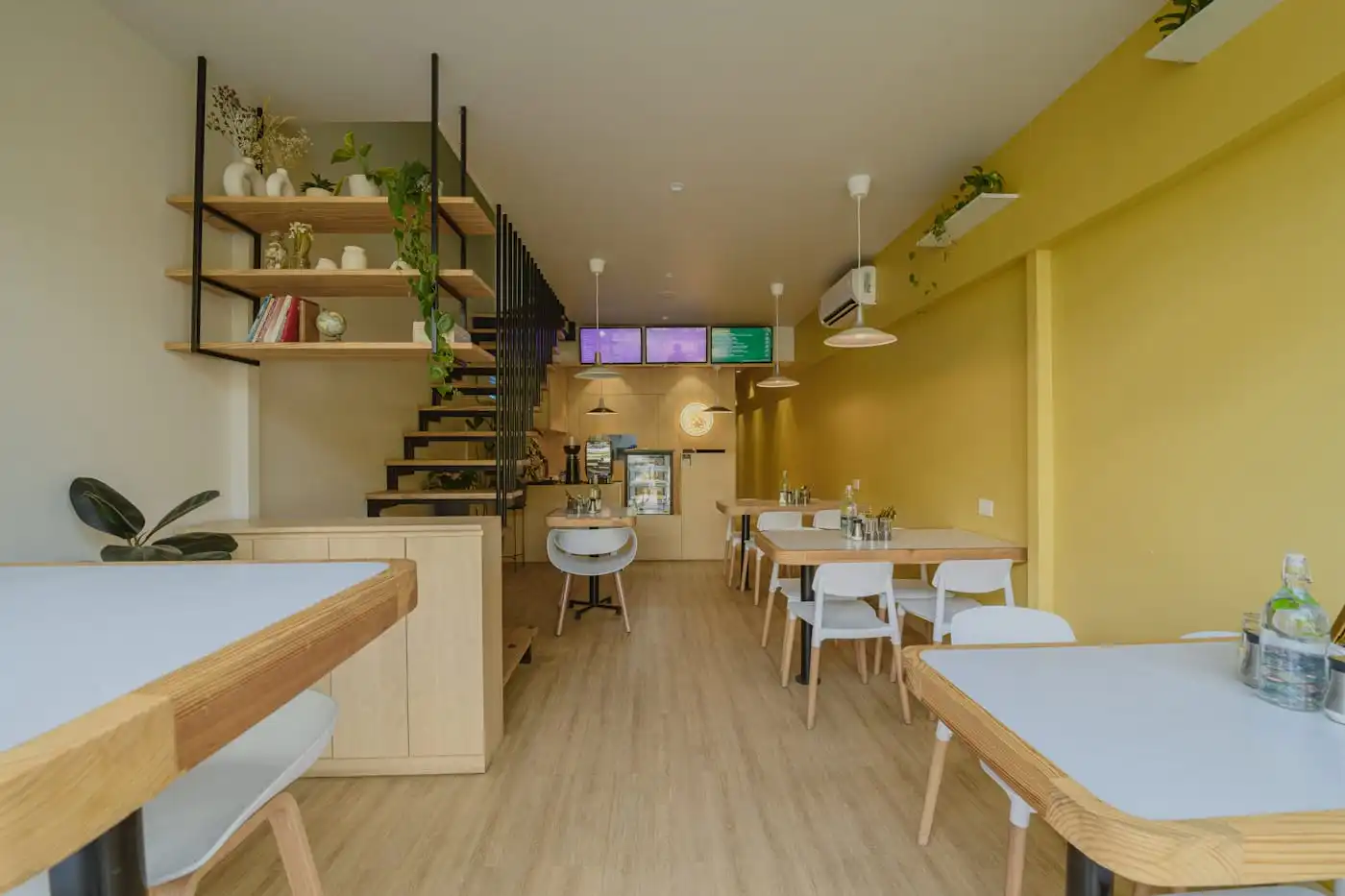 Café with a yellow wall, timber tables, open shelving and a service counter