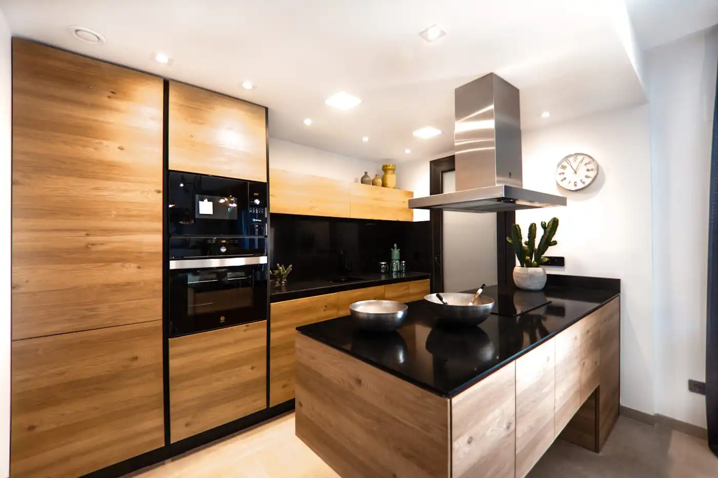 Modular kitchen with timber tall units, a black worktop and an island under a chimney hood